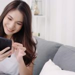 asian woman playing smartphone while lying home sofa her living room min